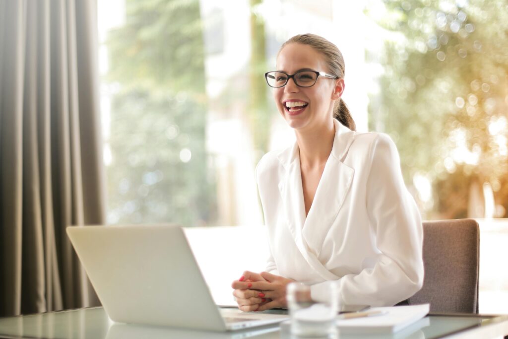 pexels-photo-3756679-3756679 Cheerful businesswoman in glasses working on a laptop, in a bright and modern office setting.